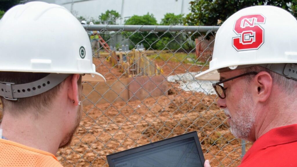 Facilities employees look at plans 
on a laptop screen while inspecting a construction site.