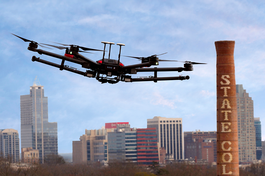 An AERPAW drone is shown flying over NC State's campus with the downtown Raleigh skyline in the background.
Photo by Marc Hall
