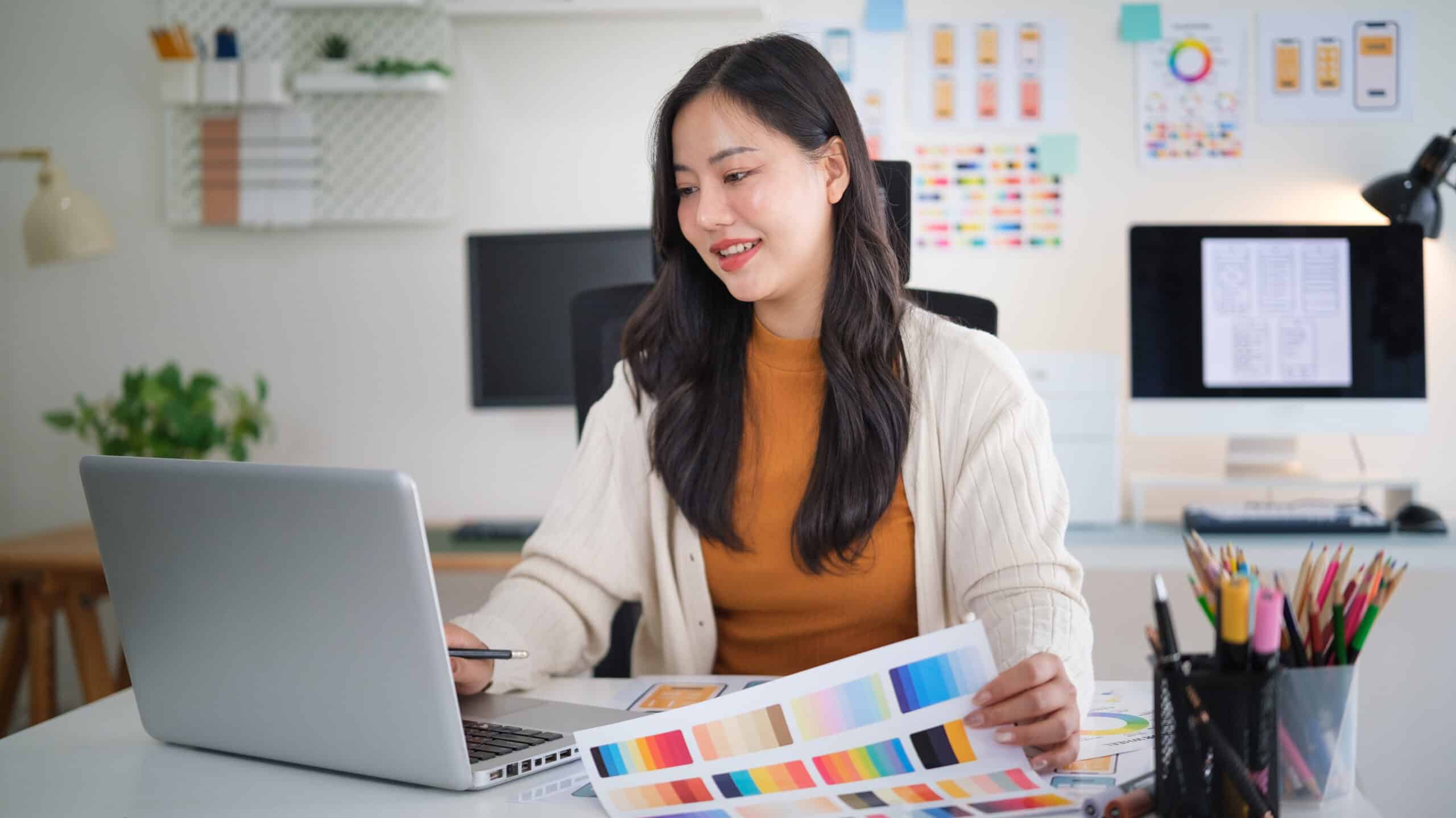 Person looks at laptop with a paper showing different colors in hand.