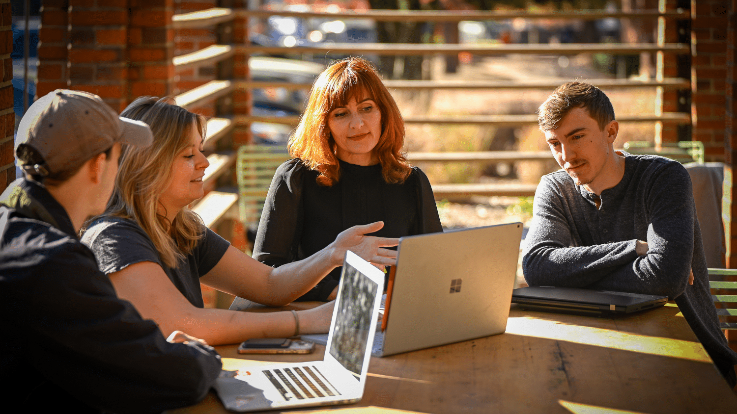 Four people chat and look at a laptop.